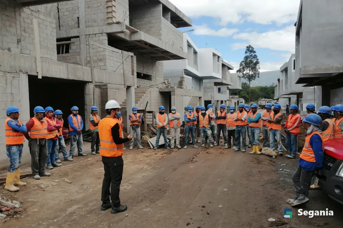 Instructor dando una charla de seguridad a una cuadrilla con casco y chaleco en una obra