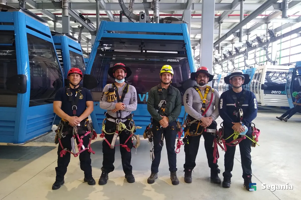 Equipo de rescate con arnés y casco frente a las cabinas de un teleférico